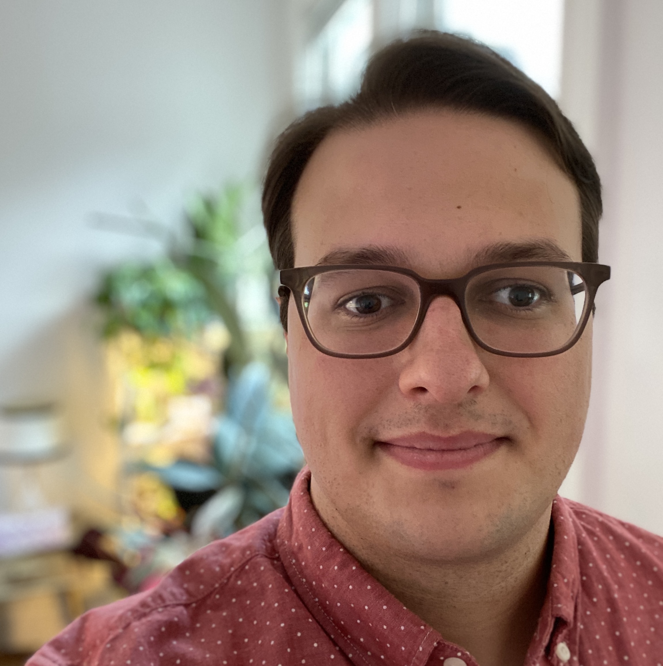 Headshot of Cole Gleason, a white man with short brown hair and glasses. Wearing a red shirt and slightly smiling.